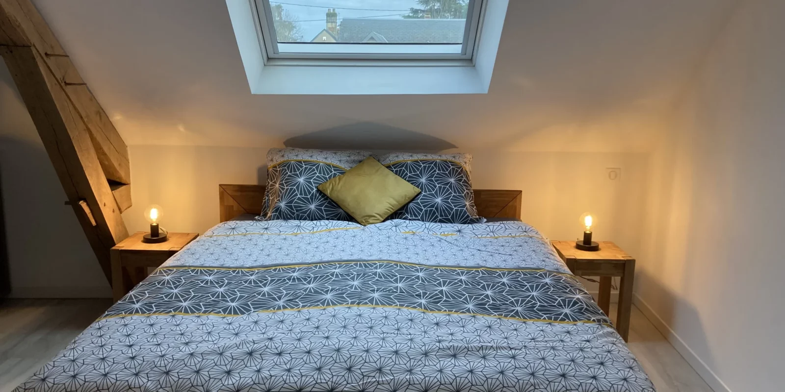 Image illustrant la chambre au deuxième étage : lit double avec table de chevet et fenêtre au dessus du lit.